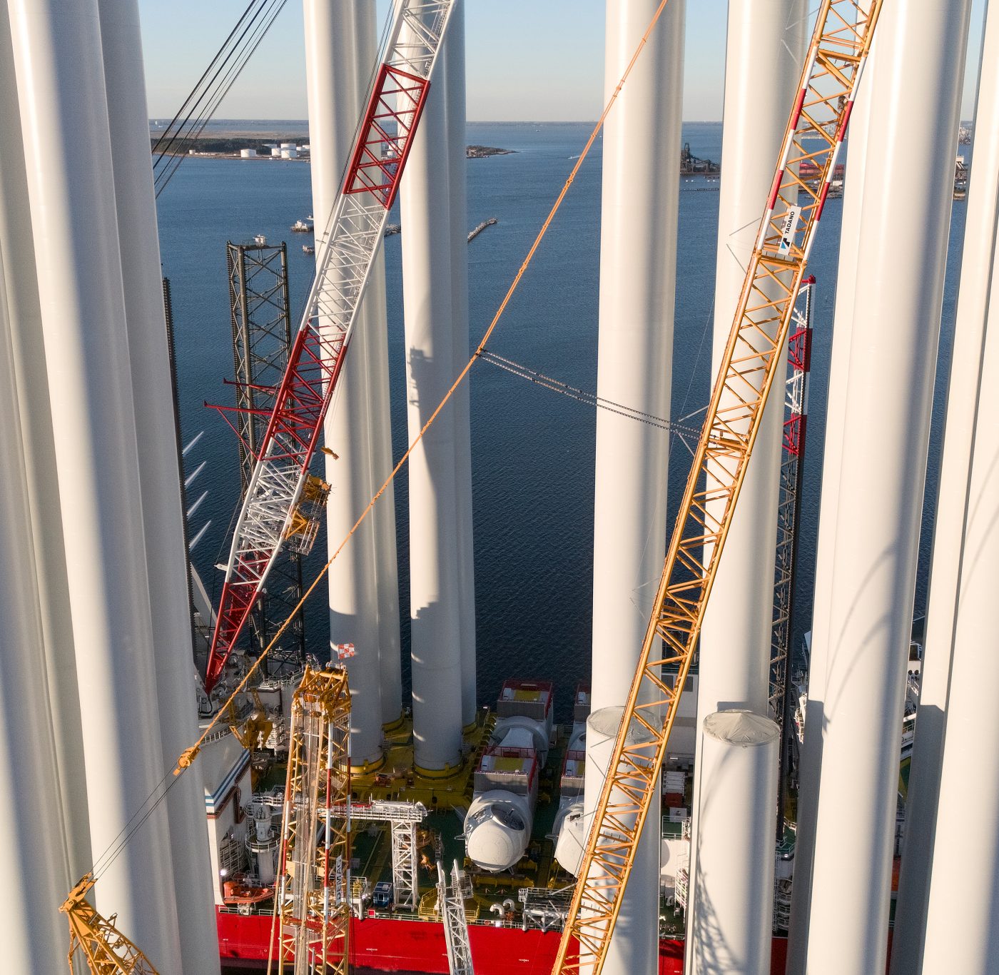Drone view of wind turbine towers and heavy cranes on offshore vessel at port