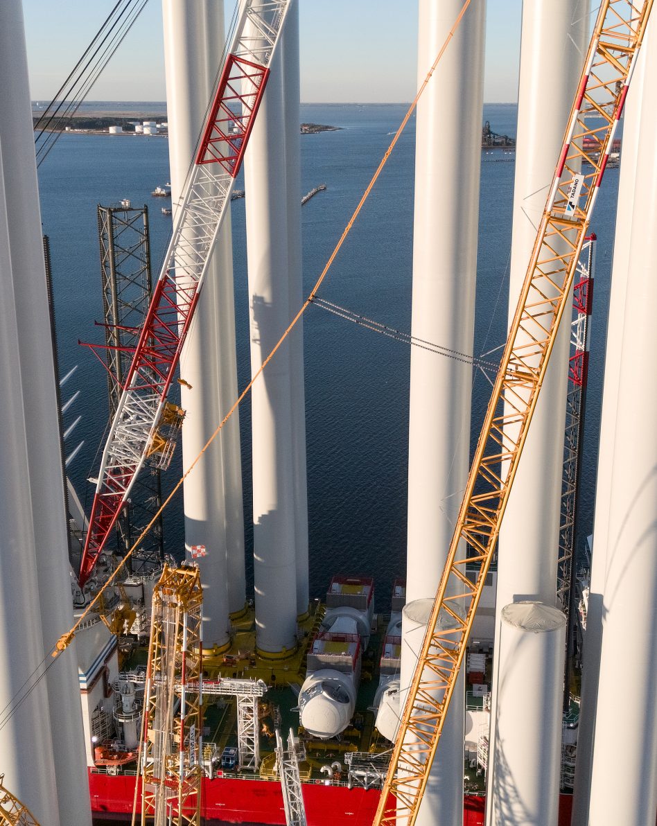 Drone view of wind turbine towers and heavy cranes on offshore vessel at port