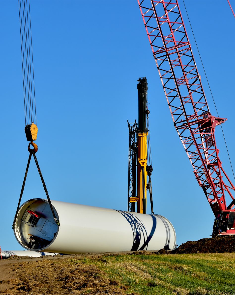 construction equipment installing base section of tower for wind turbine.